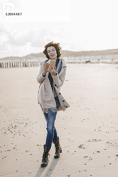 Frau am Strand mit Handy und Kopfhörer