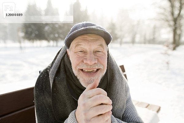 Porträt eines glücklichen älteren Mannes  der auf einer Bank in der Winterlandschaft sitzt.