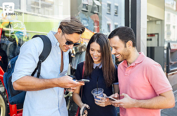 UK  London  Portobello Road  drei lächelnde Freunde beim Blick auf das Handy