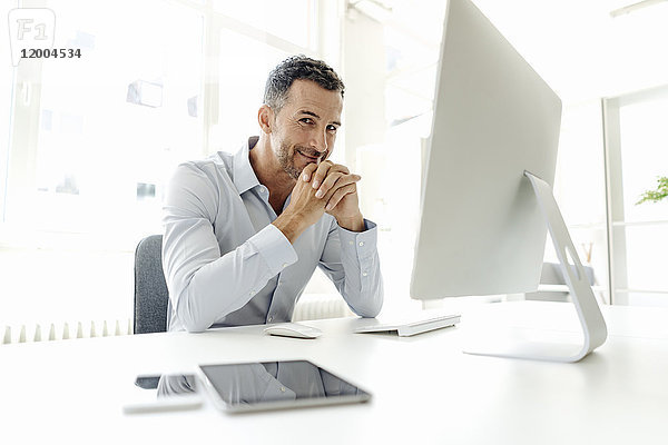 Porträt eines lächelnden Geschäftsmannes am Schreibtisch im Büro