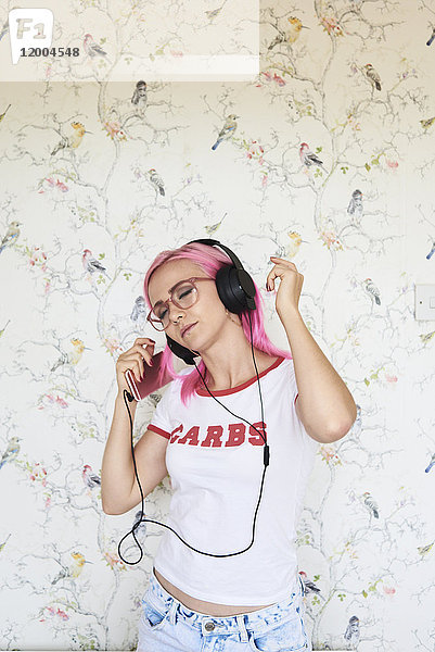 Enthusiastische junge Frau mit rosa Haaren  die zu Hause Musik hört.