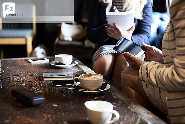 Zwei Geschäftsfrauen mit Tablette und Notizbuch bei einem Treffen in einem Coffee-Shop