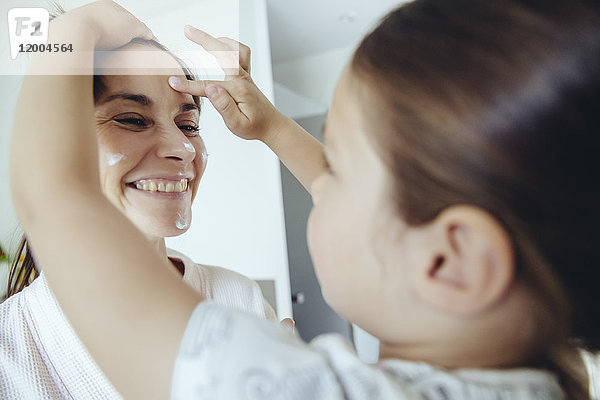 Tochter legt Gesichtscreme auf das Gesicht der Mutter
