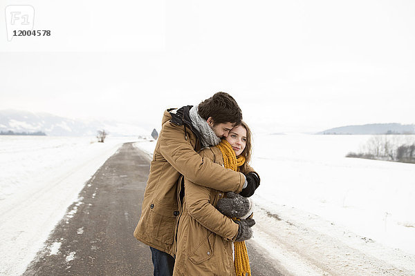 Verliebtes junges Paar steht auf der Landstraße in verschneiter Landschaft