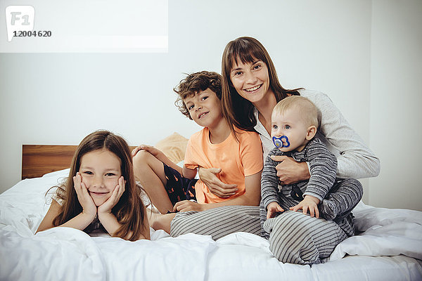 Glückliche Mutter im Bett mit ihren drei Kindern