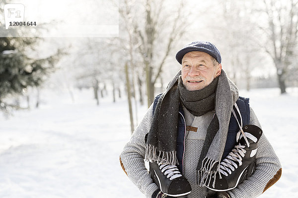Lächelnder Senior mit Schlittschuhen im Winterwald