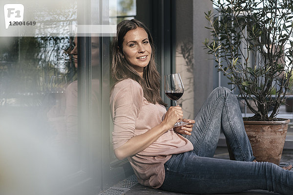 Frau mit einem Glas Rotwein entspannt auf dem Balkon