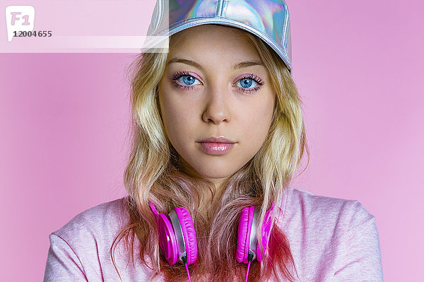 Portrait einer jungen Frau mit Kopfhörer und Basecap vor rosa Hintergrund