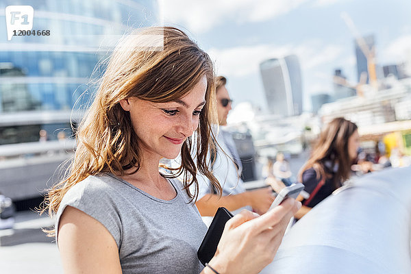 UK  London  lächelnde Frau beim Überprüfen ihres Smartphones