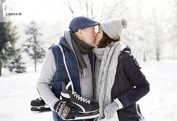 Seniorenpaar mit Schlittschuhen beim Küssen in der Winterlandschaft