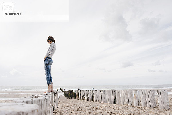 Frau auf Holzpfahl am Strand stehend