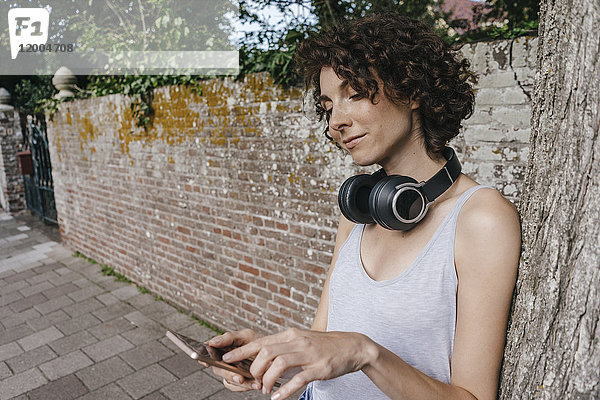 Frau mit Kopfhörer und Handy auf dem Bürgersteig