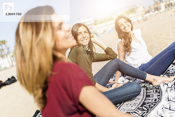 Drei glückliche Freundinnen sitzen am Strand