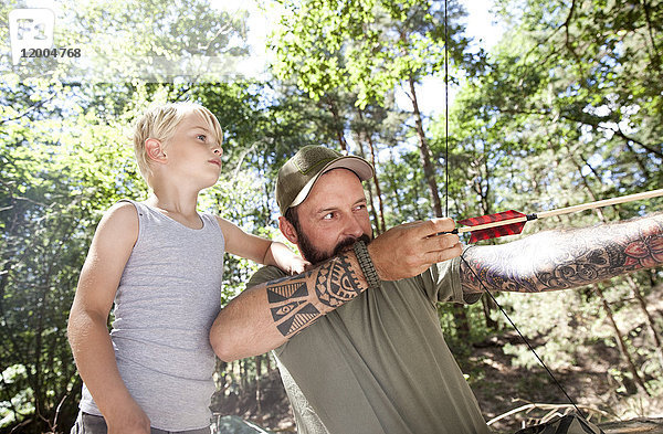 Sohn beobachtet Vater beim Schießen mit Pfeil und Bogen im Wald