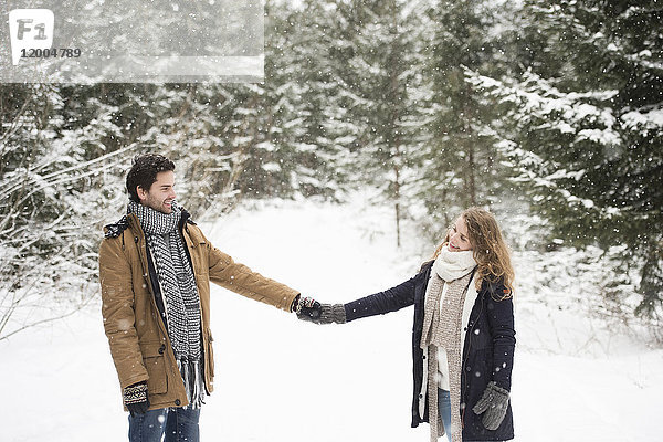 Glückliches junges Paar steht Hand in Hand in der Winterlandschaft und schaut sich an.