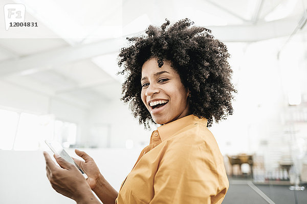 Porträt einer glücklichen jungen Frau mit einem Handy im Büro