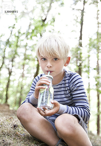 Junge  der aus einem Glas Wasser im Wald trinkt.
