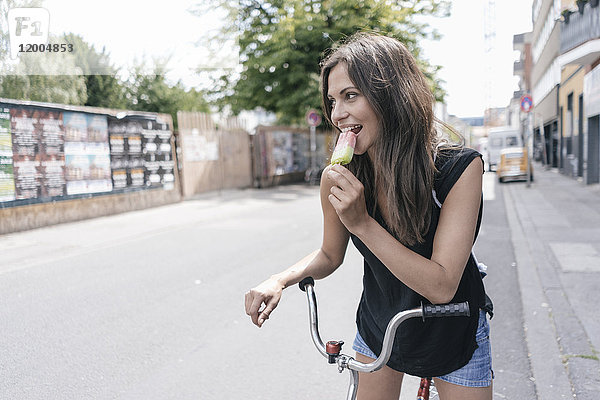 Frau mit Fahrrad isst Eis am Stiel