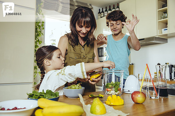 Mutter und Kinder legen Früchte in einen Smoothie-Mixer