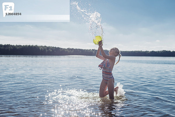 Mädchen spritzt mit Wasser am Seeufer