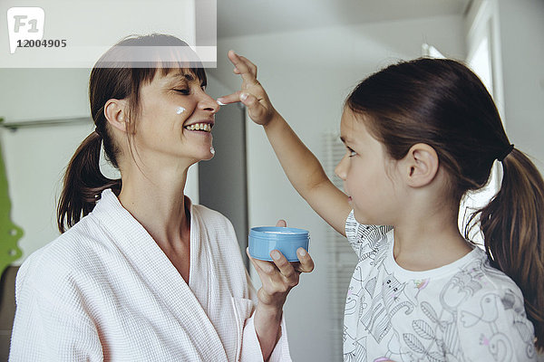 Tochter legt Gesichtscreme auf das Gesicht der Mutter