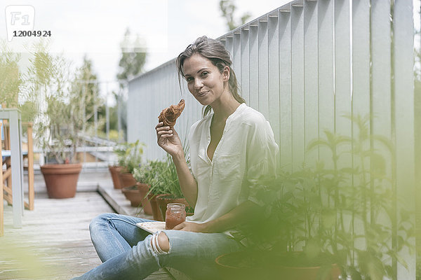 Lächelnde Frau isst Croissant mit Marmelade auf dem Balkon