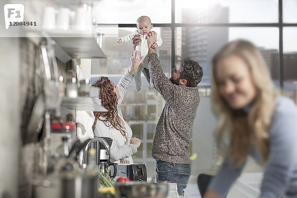 Mann und Frau heben das Baby in der Küche mit der Frau im Vordergrund auf