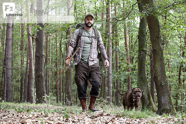 Mann mit Pfeil und Bogen spazieren mit Hund im Wald