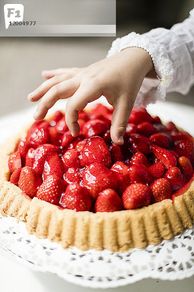 Mädchenhand nimmt Erdbeere vom Kuchen