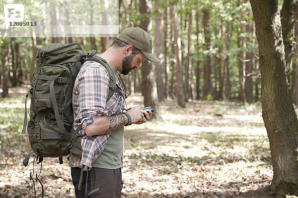 Mann mit Rucksack auf einer Wanderung im Wald per Handy