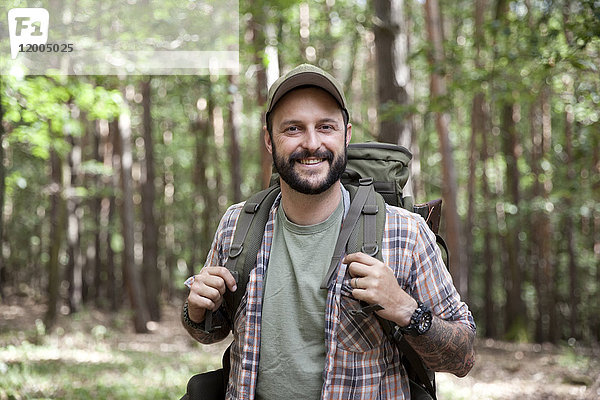 Porträt eines lächelnden Mannes mit Rucksack auf einer Wanderung im Wald