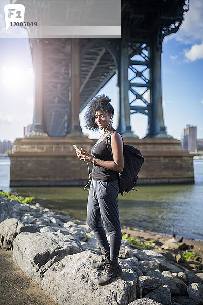 USA  New York City  Brooklyn  lächelnde Frau beim Musikhören unter der Manhattan Bridge
