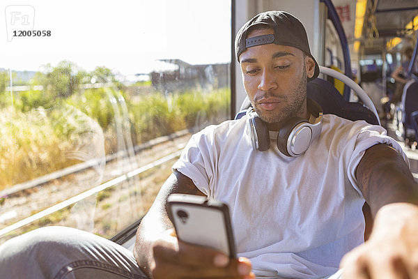 Portrait eines jungen Mannes in der Straßenbahn mit Blick auf das Smartphone