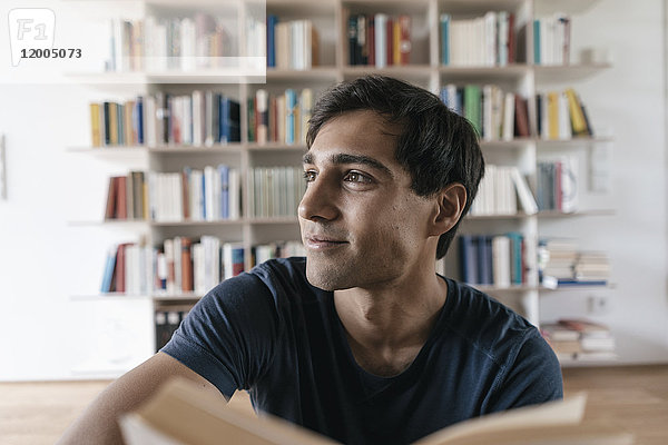 Lächelnder junger Mann mit Buch zu Hause  seitwärts schauend