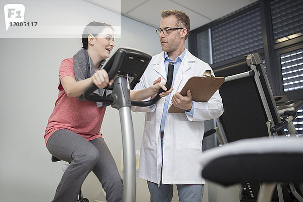 Arzt im Gespräch mit dem Patienten am Trainingsgerät