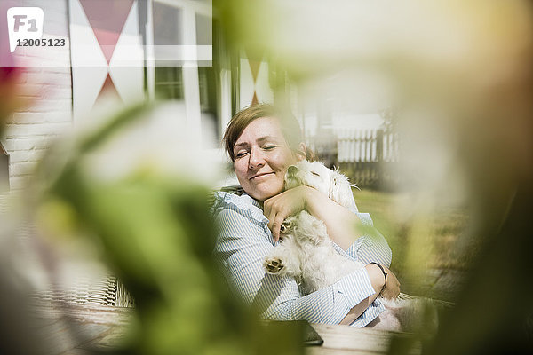 Frau kuschelt mit Hund auf der Terrasse