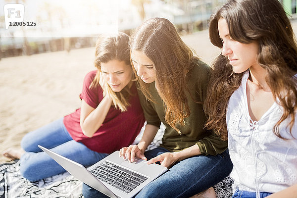 Drei Freundinnen mit einem Laptop am Strand