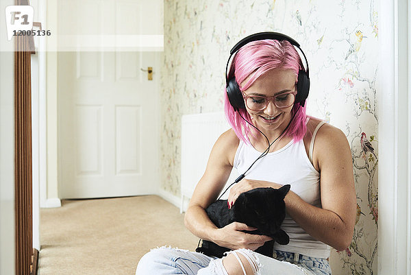 Glückliche junge Frau mit schwarzer Katze  die zu Hause Musik hört.