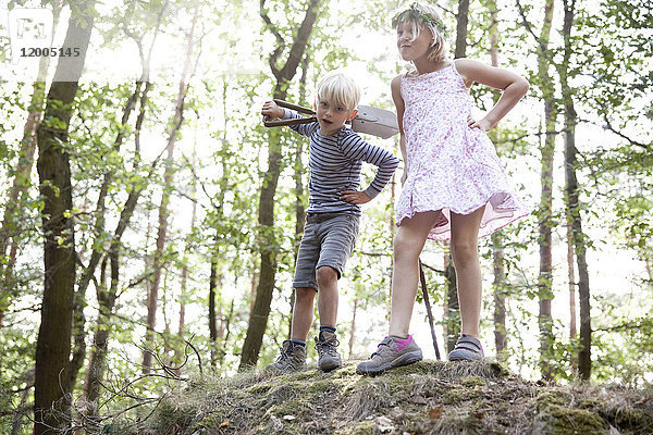 Junge und Mädchen stehen im Wald auf einem Hügel mit dem Spaten.