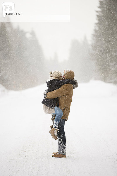 Glückliches junges Paar von Angesicht zu Angesicht in verschneiter Winterlandschaft