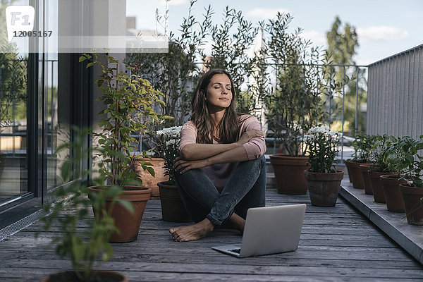 Frau mit Laptop auf dem Balkon sitzend