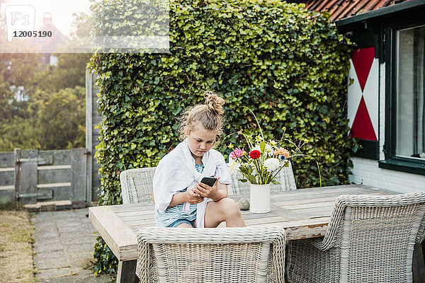 Mädchen sitzend auf dem Terrassentisch mit Handy