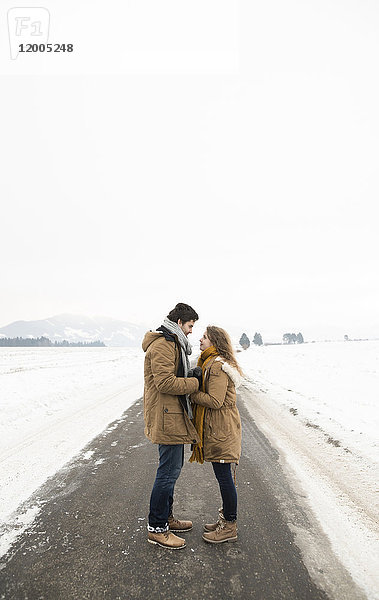 Verliebtes junges Paar steht auf leerer Landstraße in verschneiter Landschaft