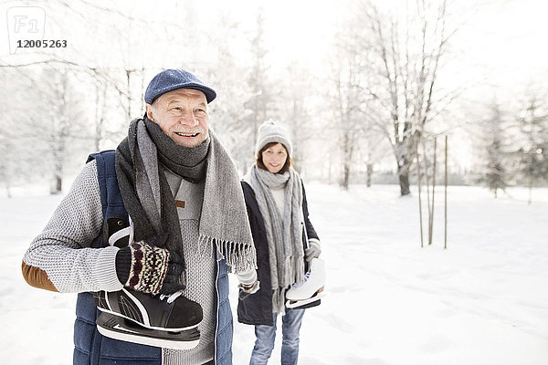Glückliches Seniorenpaar mit Schlittschuhen in der Winterlandschaft