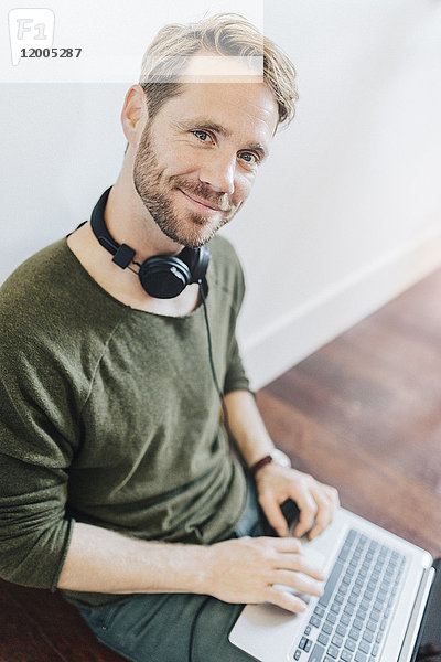 Porträt eines lächelnden Mannes mit Kopfhörer und Laptop