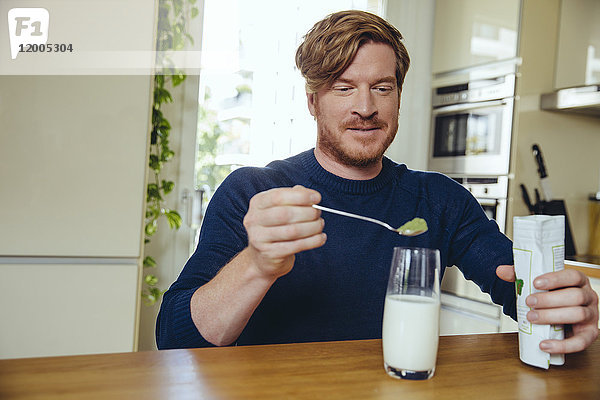 Der Mensch  der gesunde grüne Substanz in ein Glas Milch gibt.