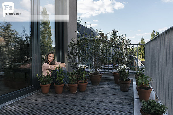 Lächelnde Frau entspannt auf dem Balkon  umgeben von Pflanzen