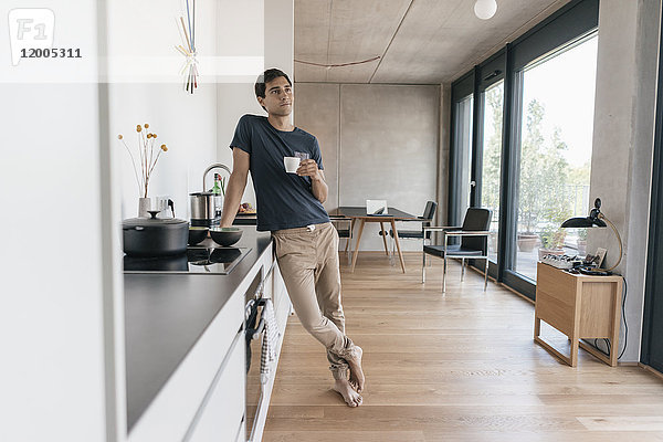 Junger Mann mit einer Tasse Kaffee in der Küche zu Hause