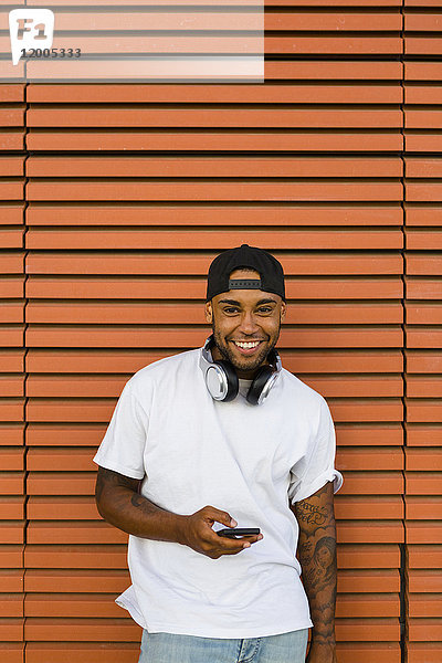 Porträt eines lachenden jungen Mannes mit Kopfhörer und Smartphone