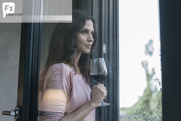 Lächelnde Frau hält ein Glas Rotwein und schaut aus dem Fenster.